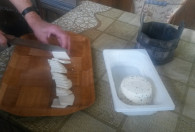 Zdjęcie przedstawia krojenie na kawałki sera koziego
