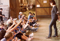 Zdjęcie przedstawia wykładowcę z dziećmi podczas zajęć w oborze